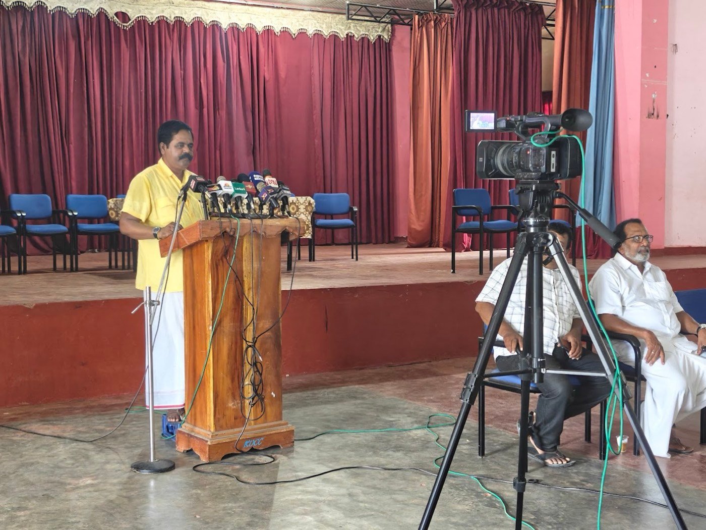 A press conference speaker at a podium filmed on a tripod camera