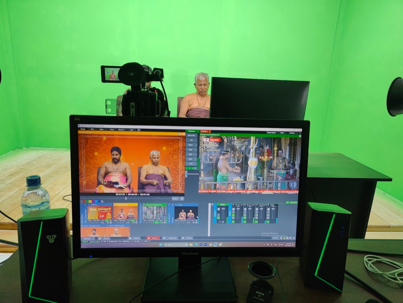 Live broadcast software on screen while two priests are filmed in the green-screen studio