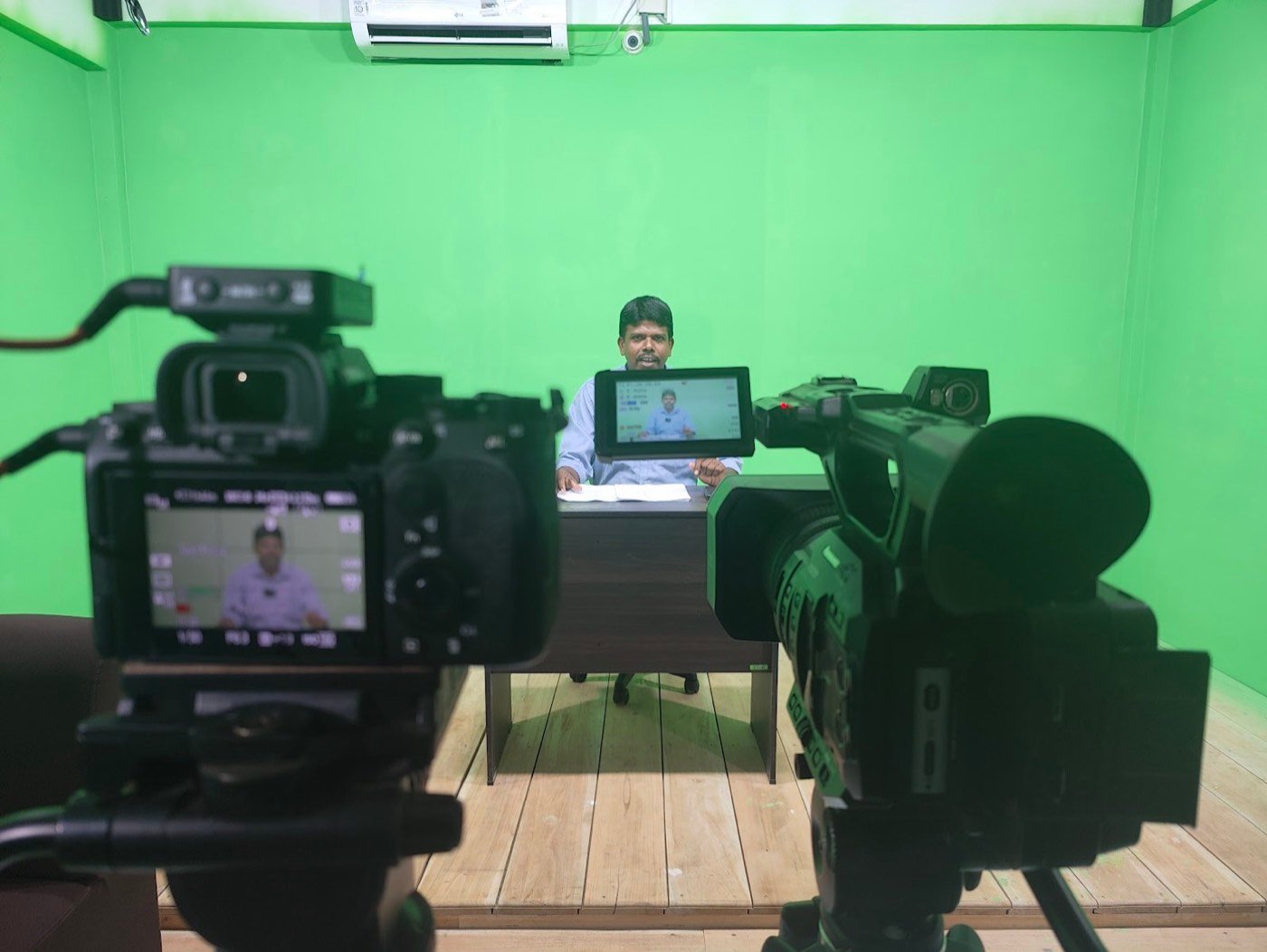A presenter at a desk recorded by two cameras in the studio